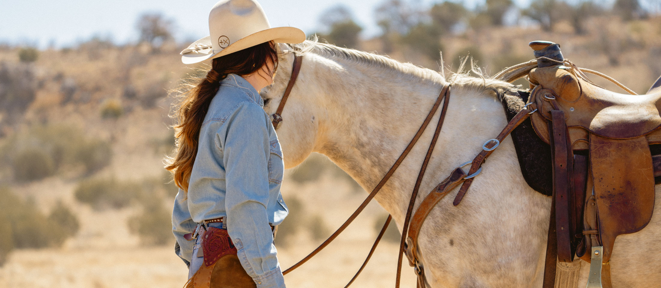 A woman wearing a cowboy hat while standing next to a horse.